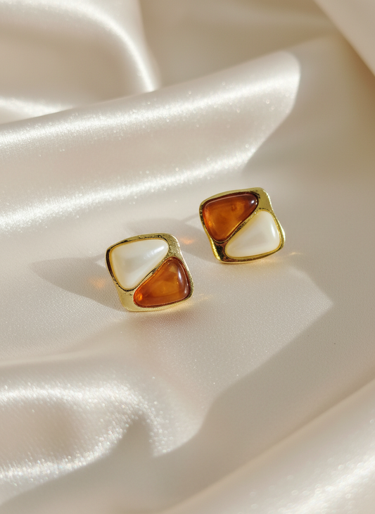 Elegant amber and cream two-tone square stud earrings displayed on luxurious satin cloth