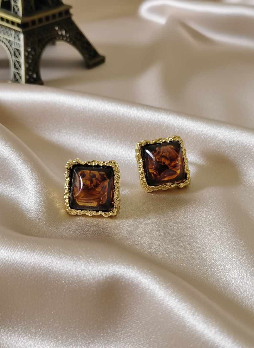 Elegant amber square stud earrings with ornate gold frames displayed on luxurious satin cloth