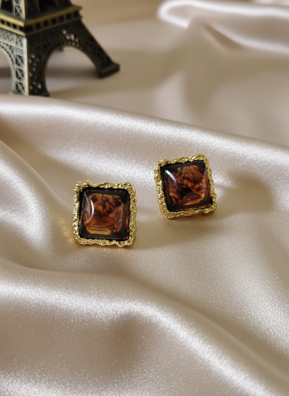 Elegant amber square stud earrings with ornate gold frames displayed on luxurious satin cloth