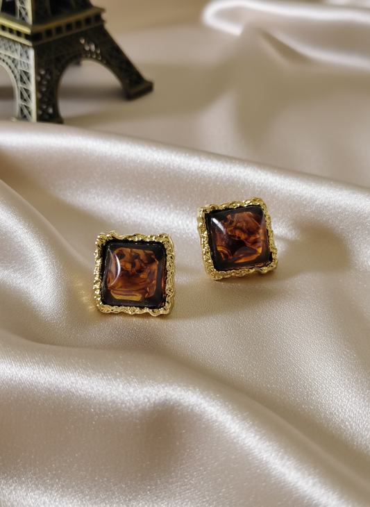 Elegant amber square stud earrings with ornate gold frames displayed on luxurious satin cloth