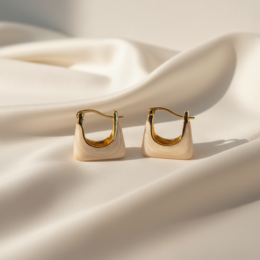Elegant beige triangular hoop earrings displayed on light satin cloth