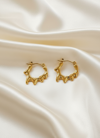 Gold melting hoop earrings on ivory satin